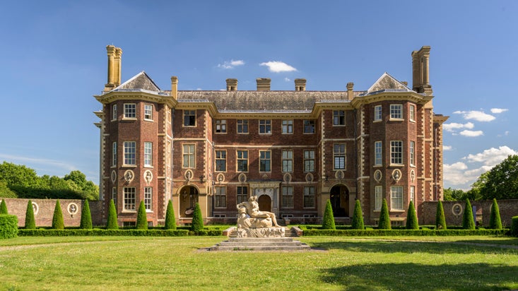 The North front and forecourt with a statue surrounded by grass at Ham House, Surrey with blue sky above